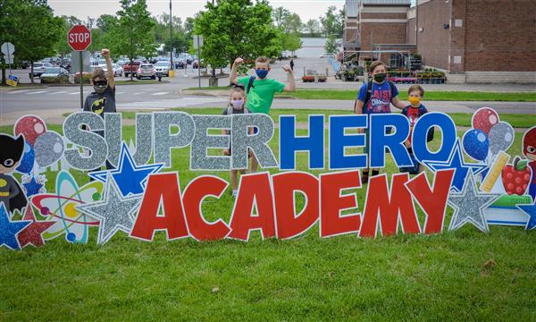 People pose next to superhero sign